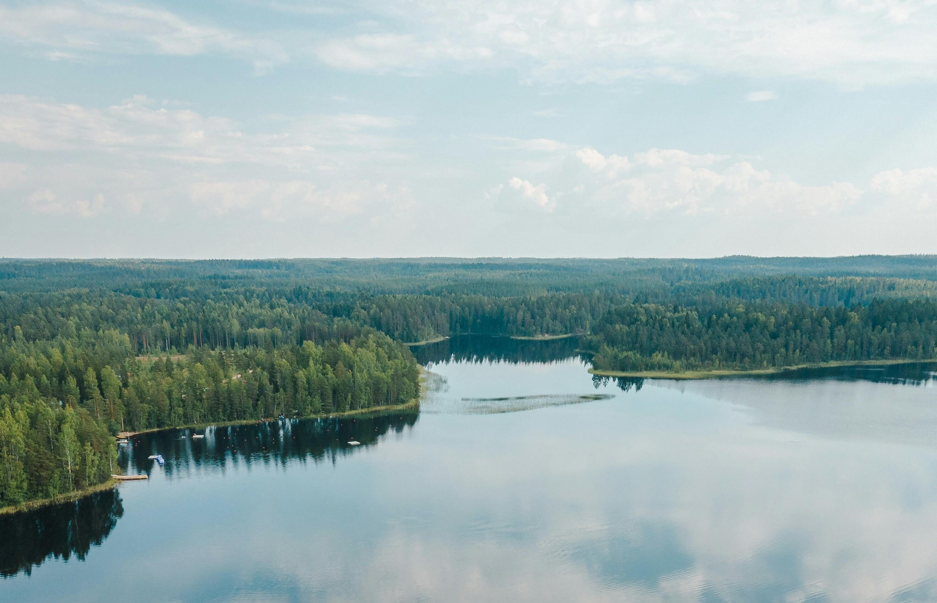 Maaginen näkymä Saimaalle Suomessa: kirkkaimmat ja syvimmät vedet, joita ympäröi tiheä metsä, heijastaen sinistä taivasta ja pilviä.